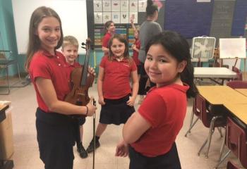 Sara Spolski, grade four, demonstrates the violin to, from left, second-graders Evan Schimpf, and Madyson Donton, and first-grader Lynn Nguyen at St. Ambrose School, Schuylkill Haven. (Photo courtesy of St. Ambrose School)