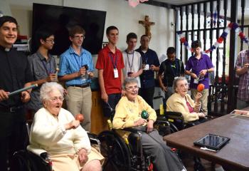 Holy Family Manor residents, from left front, Clare Farrel, Rose Donchez and Elizabeth Mrowinski enjoy playing in the Rhythm Band July 18 with seminarian Giuseppe Esposito, back left, and Quo Vadis participants. (Photo by John Simitz)