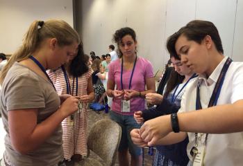 IHM postulant Beth Bartholomew, right, teaches a group of Fiat campers how to make knotted nylon rosaries. (Photo courtesy Sister Rose Mulligan, IHM)