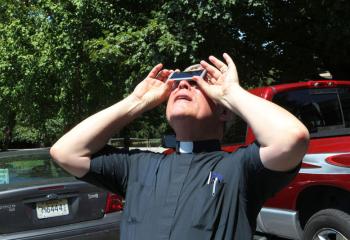 Father Richard Meredith, pastor of Sts. Peter and Paul School in Hopkinsville, Ky., catches the partial phase of the total solar eclipse on parish grounds Aug. 21. The town was near the point of maximum eclipse. (CNS photo/Dennis Sadowski) 