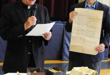 Father Joseph Tobias, left, and Terry Dunne reveal the contents of a time capsule that was secured in the cornerstone of the original church structure. Some of the contents were photos of the local congressman and pastor, letters, and architectural drawings of the church.