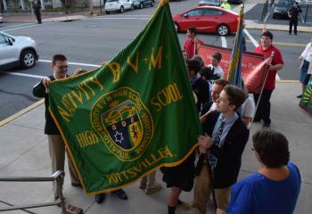 Students from Nativity BVM High School, Pottsville lift their school flag before processing into St. Clare Church. 
