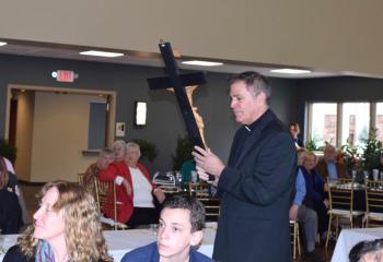 Father Philip Rodgers, pastor, carries a crucifix to be mounted in the parish hall.