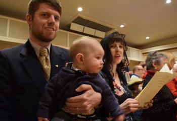 Nathaniel Menendez holds son Benedict while mom Kelly sings in the choir before Mass.