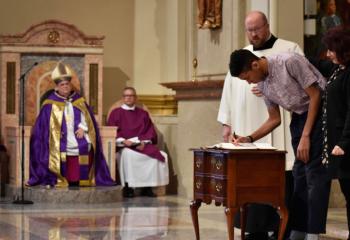 Bishop Schlert, left, witnesses a catechumen with his godmother sign the Book of the Elect.
