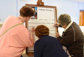 Parishioners sign a poster in tribute to Father Finlan and his call to the religious life.