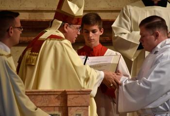 Candidate Zachary Wehr places his hands in Bishop Alfred Schlert’s hands as he makes his promise of obedience. At far left is Deacon John Hutta.