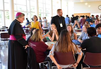 Bishop Alfred Schlert chats with families at a barbecue dinner cookout in DeSales University Center after the July 15 afternoon liturgy.