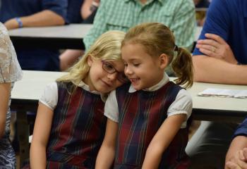 Shawna Hildebrand, left, and Lillian Porumba, first grade classmates, sit together at the Mass.