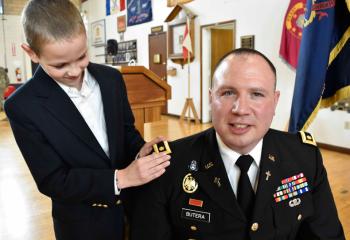 Father Christopher Butera receives epaulets from his godson Keegan Damitz, during the Promotion Ceremony elevating him to the rank of major.