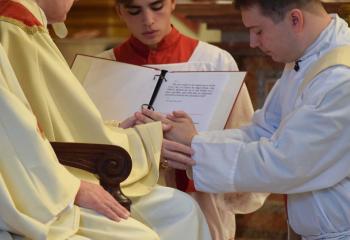 Father Rother, right, kneels before Bishop Cullen and promises respect and obedience to his ordinary during the Promise of Obedience. (Photo by John Simitz)