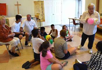 Janice Stavrou teaches a science class to children after breakfast, as Mary Spieker, left, and Deacon Thomas Reimer, back right, sit in on the class. (Photo by John Simitz)