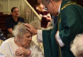 Bishop Schlert anoints Betty Begley with blessed oil while performing the Sacrament of the Anointing of the Sick.