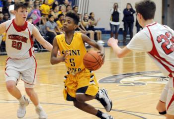 St. Peter’s Josiah Jordan (5) drives the ball between St. Thomas More’s Brendan Boyle (20) and Griffin Patridge (22) during the grade school boys’ championship.  