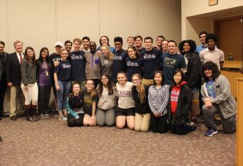 Thomas Awiapo, standing center, embraces DeSales’ students and staff including Father Tim McIntire, chaplain, left, and Robert Olney, director of the Diocesan Office of Marriage and Natural Family Planning, second from left, after discussing the importance of supporting CRS. (Photo courtesy of Robert Olney)