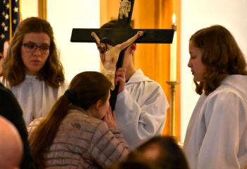 A girl adores Christ by kissing him and the cross he was crucified on.