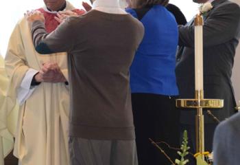 Among those praying over Father Greenfield as he is entrusted with the mission of DeSales University are, from left: Gerry Greenfield, brother; Mary Gotzon, administrative assistant to the president; LaShara Davis, assistant professor of communication (hidden); and Matt Trovato, DeSales student and candidate for the Oblates of St. Francis de Sales.