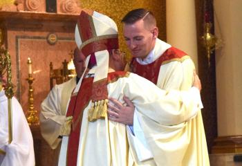 Bishop Schlert, left, embraces Father Hutta during the Kiss of Peace.