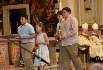 Father Hutta’s niece and nephews present the offertory gifts during the Mass. From left are John Jacob Klein, Andi Jean Girard, and Jacob and Joshua Shelton.