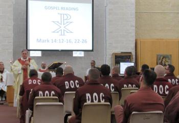 Bishop Schlert delivers the homily during the evening liturgy. Behind him are Father Stokes and inmates who served at the Mass.