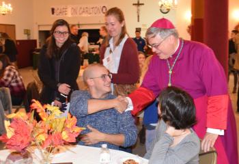 Bishop of Allentown Alfred Schlert, right, greets Dominic and Helen Behe at a social for young adults in the parish hall.