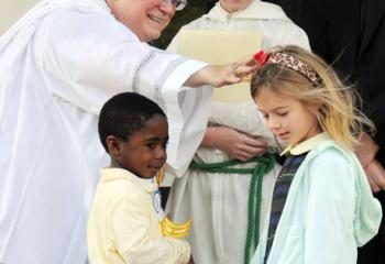 Bishop Alfred Schlert bends to bless kindergarten student Tessa Shelly after she and classmate Morris Massaquoi gave the Bishop a thank-you card with a picture of the Early Learning Center and their names. Watching are, from left, Tanner McQueen, Monsignor Vincent York and Father Stephen Maco.