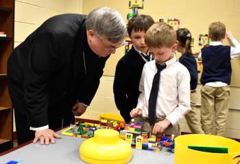Bishop Schlert admires a Lego project created by St. Jerome Regional School first grade students Tanner Zukovich, center, and Rellan Krajcirik. (Photo by John Simitz)