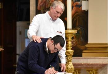 Deacon Robert Snyder, assigned to Cathedral of St. Catharine of Siena, watches Rafael Miranda sign the Book of Elect.