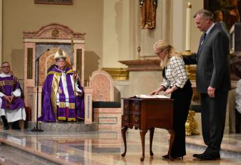 Debbie Nowotarski signs the book with sponsor Michael Nowotarski, parishioner of St. Benedict, Mohton. Witnessing the act are Deacon Isidro Rivera-Gonzalez, associate director for Hispanic Outreach for the Office of the Permanent Diaconate, left, and Bishop Schlert.