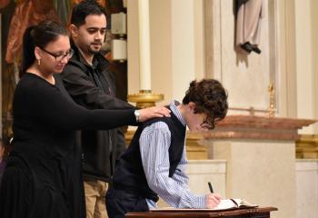 Nolbert Gomez signs the Book of Elect, signifying his commitment and discipleship, with his sponsors, Yariel Delgado and Kristin Delgado, parishioners of Holy Infancy, Bethlehem.
