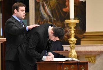 Ryan Leskoven signs the Book of Elect with guidance from his sponsor, Patrick Smith, parishioner of All Saints, McAdoo.