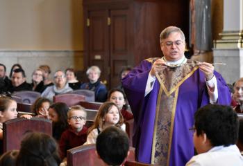 Bishop Schlert uses a spoon to explain sin and graces to the schoolchildren during his homily at the 9 a.m. Ash Wednesday Mass.(Photo by John Simitz)