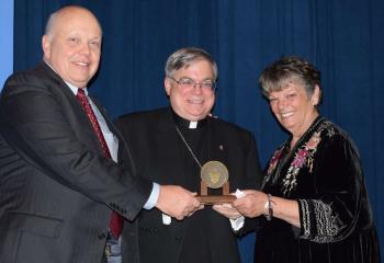 Bishop Schlert, center, presents the medallion to John and Alice Freeh.