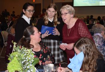 Sister Janice Marie Johnson, standing right, chats with a guest while helping student volunteers sell raffle tickets. From left are Sara Miller, LuLu Blewitt, Isabella Allen and Morgan Medvedz.