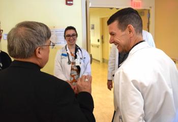 Bishop Schlert chats with Jessica Henry, Penn State physician assistant student, left, and Dr. Francis Quigley, hospitalist. During his visit Bishop Schlert celebrated Mass, had lunch, enjoyed a meet-and-greet with board members and visited patients at the Bern Township Campus.