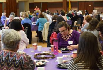 Women nosh on tasty breakfast offerings as Susan Teaford speaks at the podium.