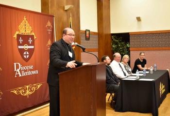 Father Eugene Ritz offers remarks as panelists listen.