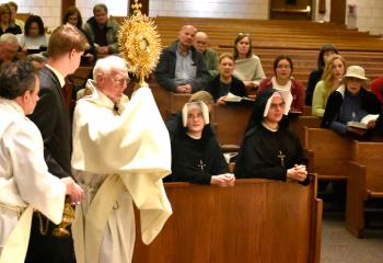 Deacon Charles Coyle, retired permanent deacon of St. Joseph the Worker, carries the monstrance in procession at the Exposition of the Blessed Sacrament. With him are, from left, Deacon Bruno Schettini of St. Joseph the Worker and Rick Dooley. Seated in the pew behind them are, from left, Congregation of the Sisters of Our Lady of Mercy Sisters Veritas Green and Gaudia Skass.