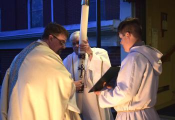 From left, Father Eric Gruber, Deacon Jack O’Connell and altar server Dominic Gorr place nails in the Pascal Candle at St. John Fisher. “This day reminds us that God triumphs over the devil. Good triumphs over evil. Even amidst some awful challenges and evils that are present in the world today, God triumphs. By his death, we have eternal life. By his death, we have something more awesome to hope for, heaven,” said Bishop Alfred Schlert. (Photo by John Simitz)