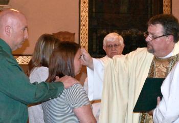 Father Eric Gruber welcomes new members of the Church through confirmation at St. John Fisher: Heather "Margaret" Ruschatz, foreground, with her sponsor, husband Todd Rushatz; and Alexis "Anne" Ruschatz with sponsor Carol Dennis. (Photo by John Simitz)