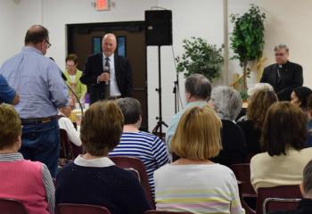 A man asks a question during the meeting at St. Catharine. Listening in front are Paul Wirth of the Diocesan Office of Communications, center, and Bishop of Allentown Alfred Schlert, right.