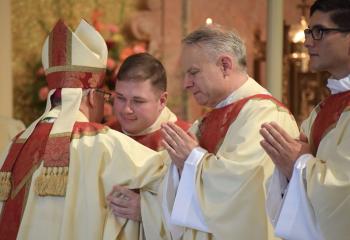 Bishop Schlert extends the sign of peace during the Kiss of Peace to Father Wehr, (Photo by John Simitz.)