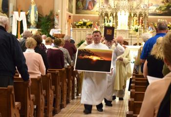 Bill Frost, minister of the altar, carries the “I’ll Remember You” sunset photo by Tami Quigley in the recessional. Behind him are, from left, Father Jim Torpey, Deacon William Urbine and Father Luigi Palmieri.