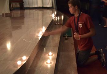 A young man places a candle before the altar at Evening Prayer during Quo Vadis.