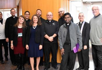 Alexa Smith, front left, and Annie Sarlo, of the Secretariat for Catholic Life and Evangelization gather with priests available for confession at the conference, from left: Father Brian Miller, Father John Hutta, Father Giuseppe Esposito, Father Stephan Isaac, Father Daniel Kravatz, Father David Anthony, Father Jojappa Adagatla, Father Anthony Mongiello and Father John Pendzick. (Photo by John Simitz)