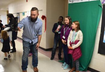 Students stand before the green screen before giving a live weather report.